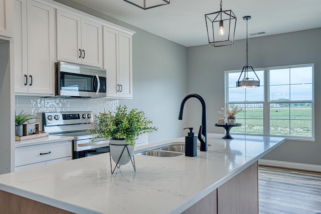 kitchen with light stone counters, hanging light fixtures, stainless steel appliances, a kitchen island with sink, and white cabinets