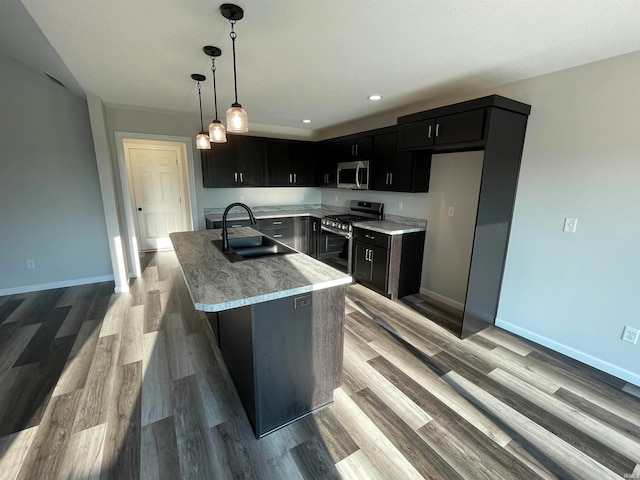 kitchen with gas range, decorative light fixtures, an island with sink, sink, and light wood-type flooring