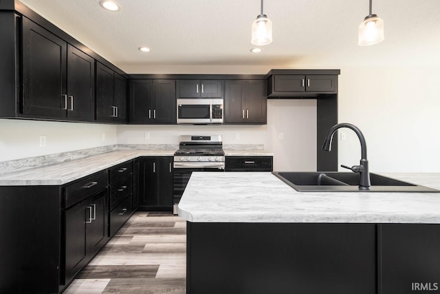 kitchen featuring sink, light wood-type flooring, stainless steel appliances, and pendant lighting