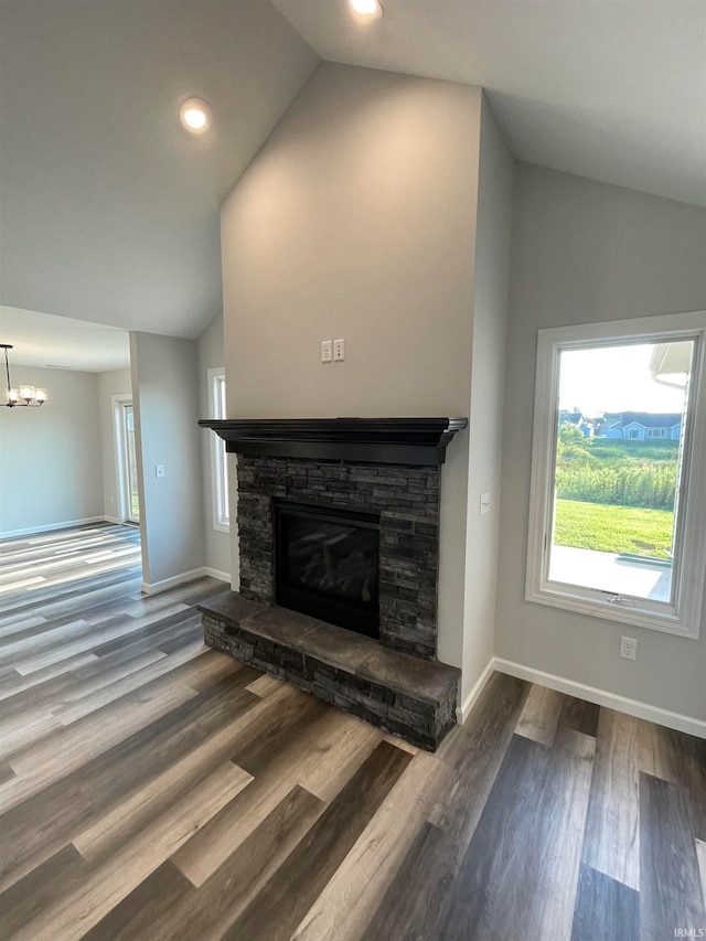 unfurnished living room featuring high vaulted ceiling, a notable chandelier, a stone fireplace, and wood-type flooring