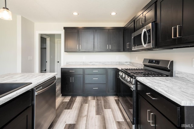 kitchen featuring sink, light stone counters, light wood-type flooring, pendant lighting, and stainless steel appliances