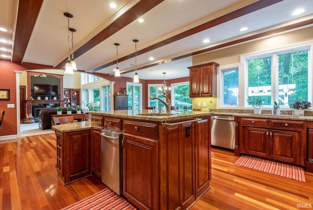 kitchen featuring hanging light fixtures, stainless steel dishwasher, sink, and a center island with sink