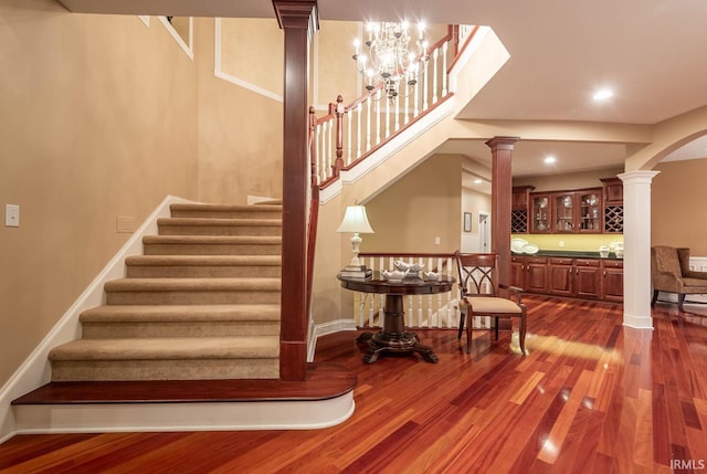 stairs featuring ornate columns, hardwood / wood-style flooring, and a chandelier