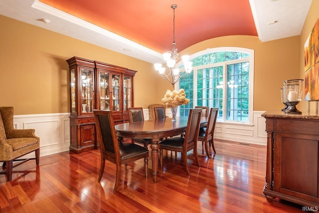 dining room featuring lofted ceiling, hardwood / wood-style flooring, a raised ceiling, and a chandelier