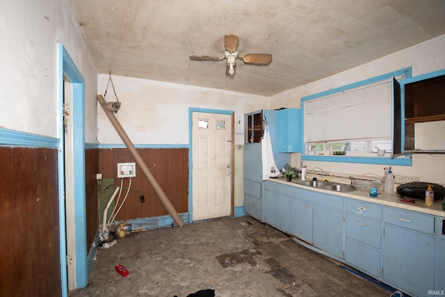 kitchen featuring a ceiling fan, a wainscoted wall, a sink, and blue cabinetry