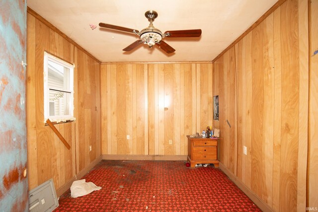 unfurnished room featuring crown molding, wood walls, a ceiling fan, and baseboards