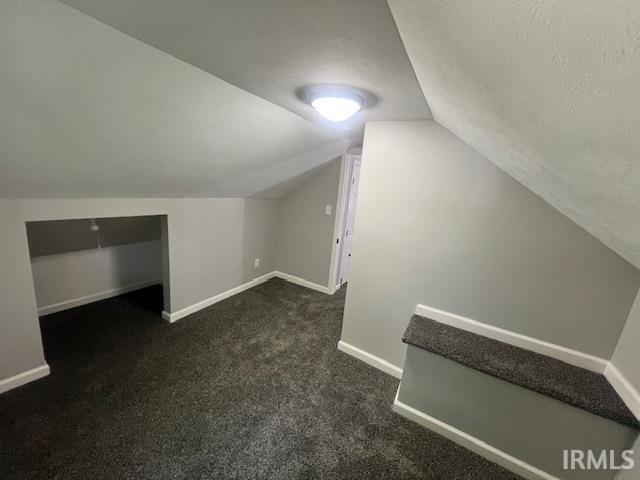 additional living space with lofted ceiling, dark carpet, and a textured ceiling