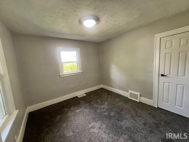 spare room with dark colored carpet and a textured ceiling