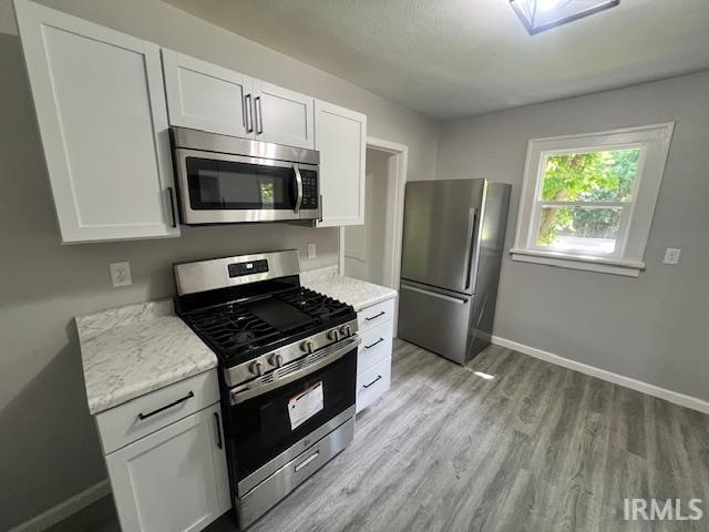 kitchen with white cabinetry, light stone counters, stainless steel appliances, and light wood-type flooring