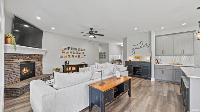 living room featuring ceiling fan, a stone fireplace, and light hardwood / wood-style floors