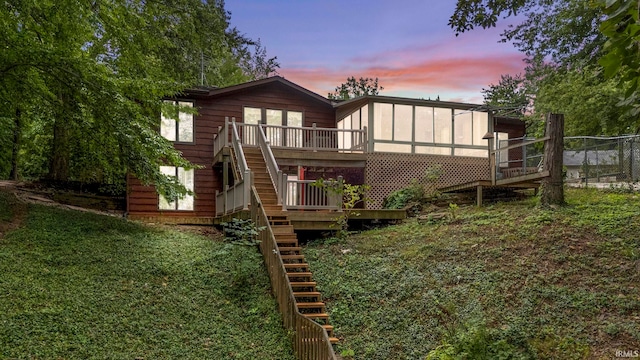 back house at dusk with a wooden deck and a lawn