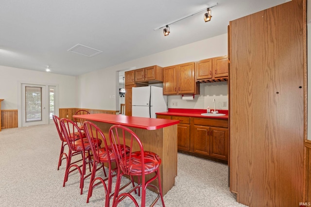 kitchen featuring a breakfast bar, rail lighting, white refrigerator, light colored carpet, and a kitchen island