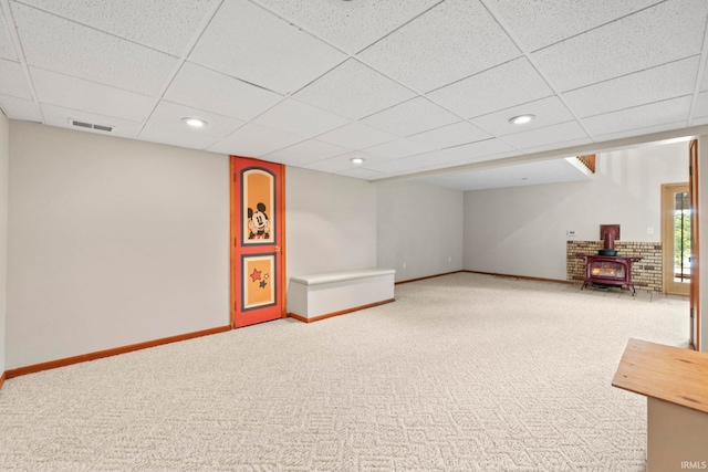 basement featuring a drop ceiling, carpet floors, and a wood stove