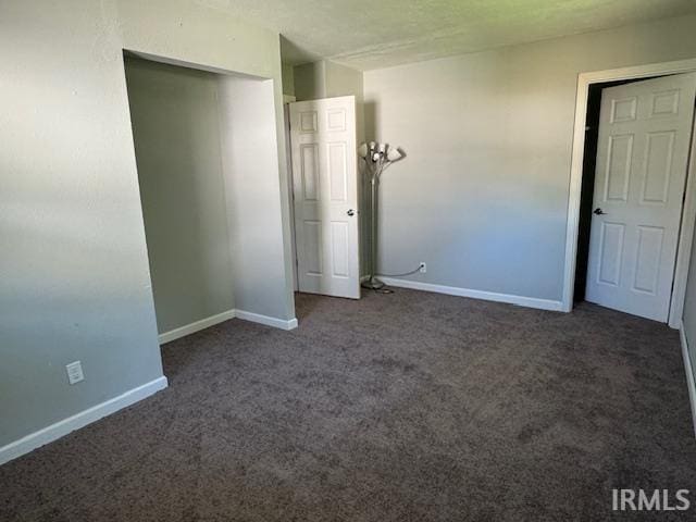 unfurnished bedroom with dark carpet and a closet