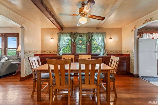 dining space with ceiling fan, hardwood / wood-style flooring, a textured ceiling, and beam ceiling