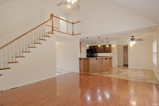 unfurnished living room with ceiling fan, a towering ceiling, and light hardwood / wood-style flooring