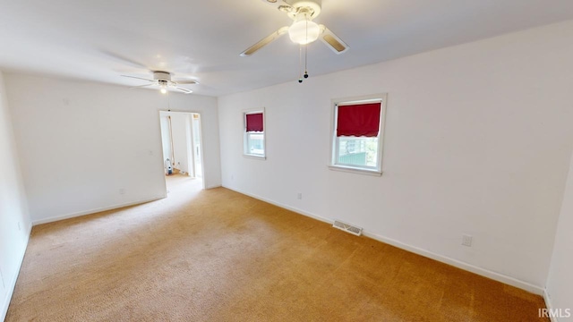 empty room featuring light carpet, ceiling fan, visible vents, and baseboards