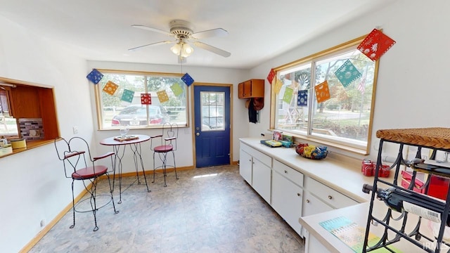 kitchen with ceiling fan, light countertops, white cabinetry, and baseboards