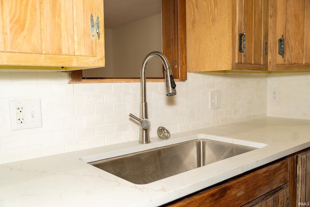 kitchen featuring decorative backsplash, sink, and light stone countertops