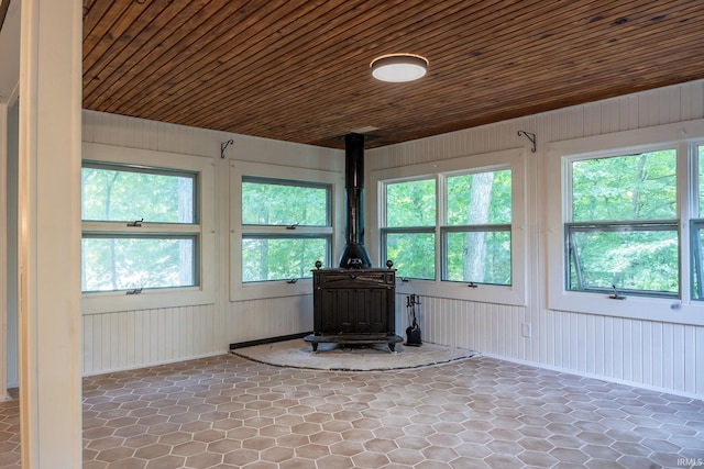 unfurnished sunroom featuring a wood stove, wood ceiling, and a healthy amount of sunlight