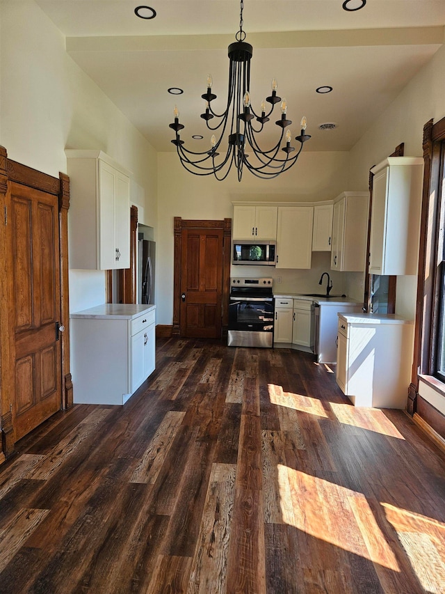 kitchen with dark hardwood / wood-style floors, hanging light fixtures, appliances with stainless steel finishes, white cabinets, and a notable chandelier