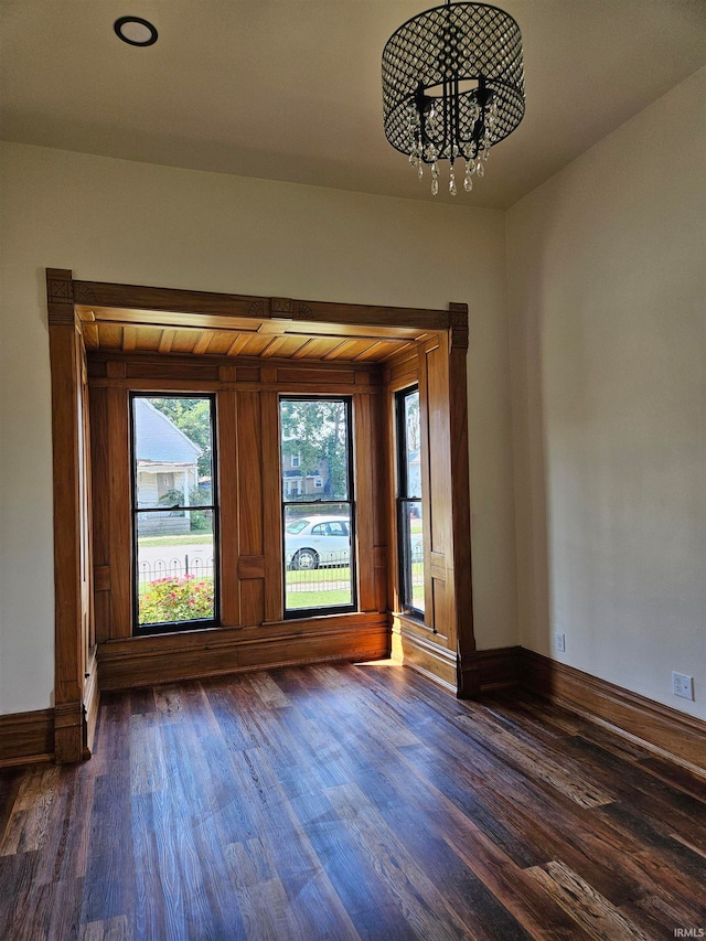 spare room with a notable chandelier and dark wood-type flooring