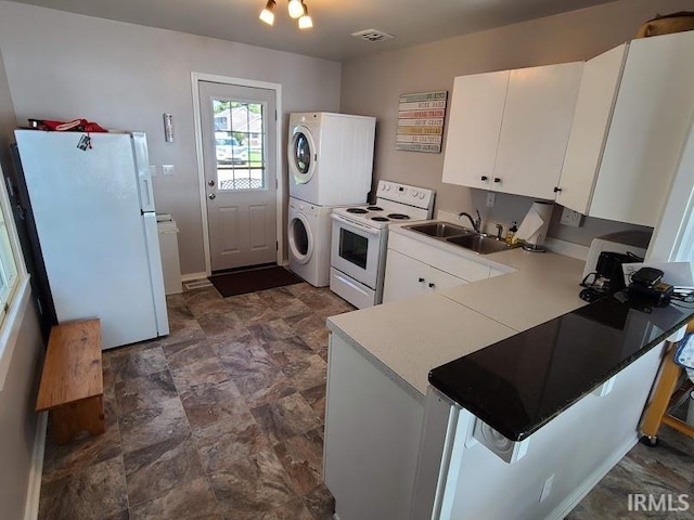 kitchen featuring sink, kitchen peninsula, white appliances, white cabinetry, and stacked washer / drying machine