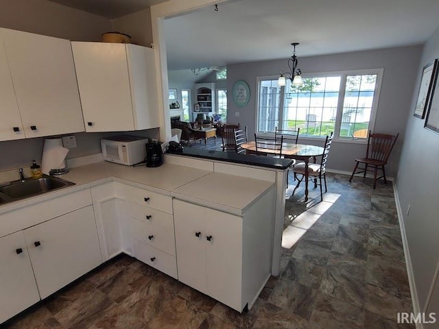 kitchen featuring kitchen peninsula, white cabinetry, pendant lighting, and a chandelier