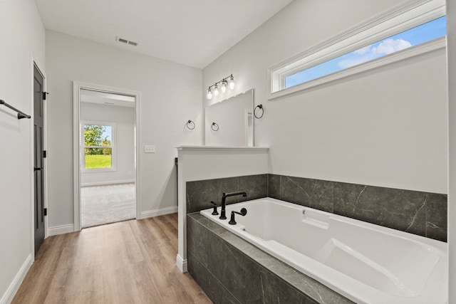 bathroom with wood-type flooring and a relaxing tiled tub