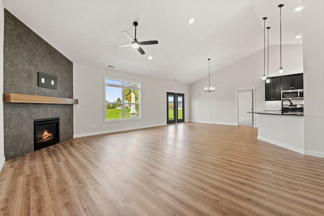 unfurnished living room featuring ceiling fan with notable chandelier, high vaulted ceiling, a tiled fireplace, and light hardwood / wood-style floors