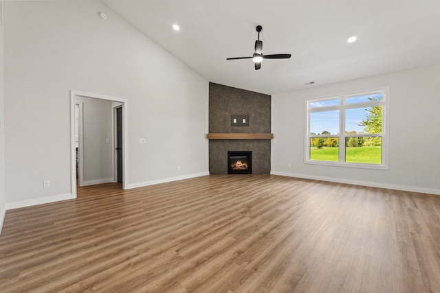 unfurnished living room featuring ceiling fan, high vaulted ceiling, light hardwood / wood-style flooring, and a tiled fireplace