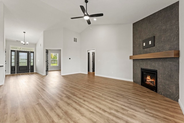 unfurnished living room with ceiling fan with notable chandelier, high vaulted ceiling, light hardwood / wood-style flooring, and a tile fireplace