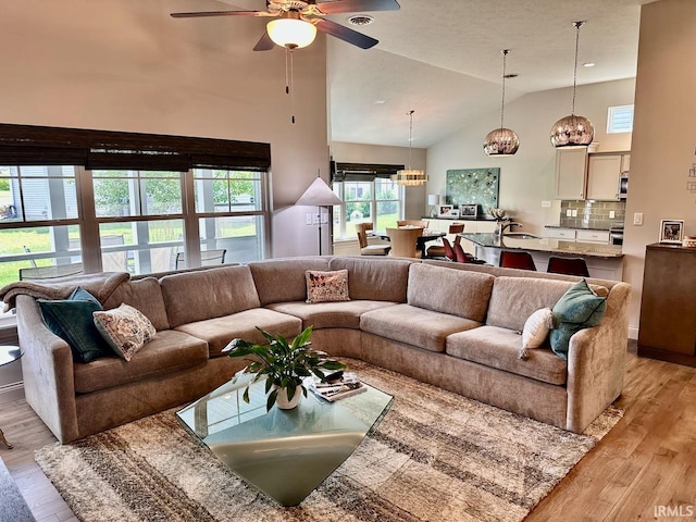 living room featuring sink, high vaulted ceiling, light hardwood / wood-style flooring, and ceiling fan with notable chandelier