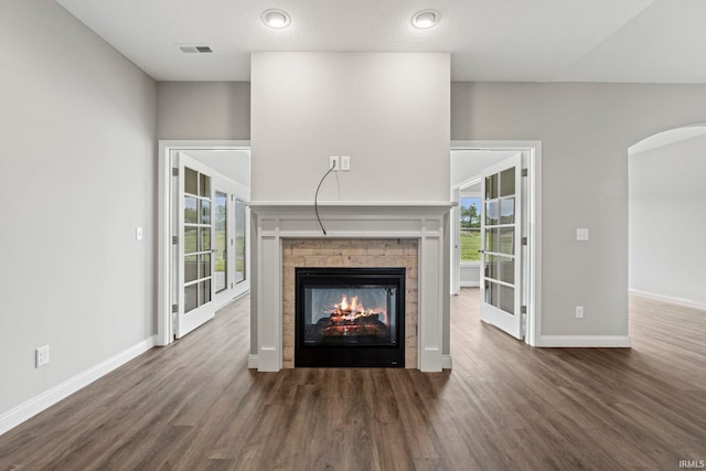 unfurnished living room featuring visible vents, baseboards, arched walkways, wood finished floors, and a stone fireplace