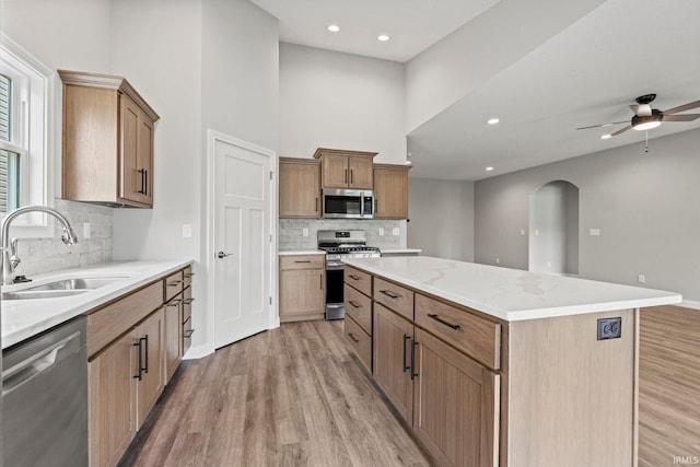 kitchen featuring a center island, arched walkways, stainless steel appliances, light wood-style flooring, and a sink