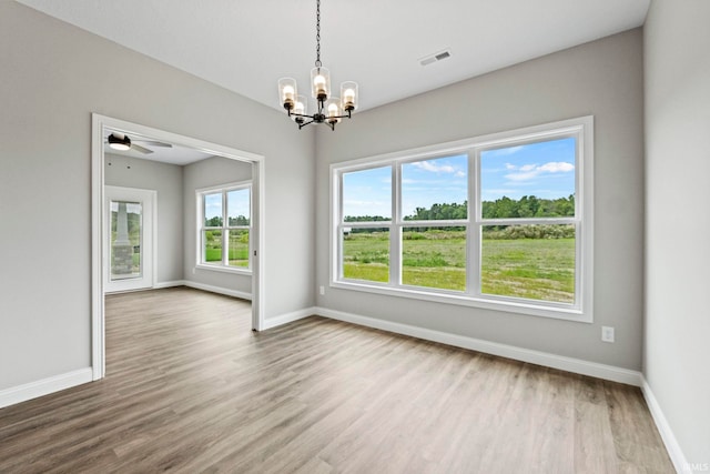 empty room with ceiling fan with notable chandelier, wood finished floors, visible vents, and baseboards