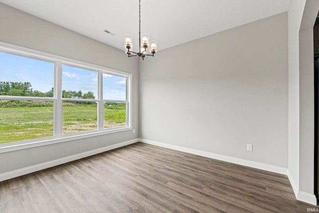 spare room with a notable chandelier, visible vents, baseboards, and wood finished floors