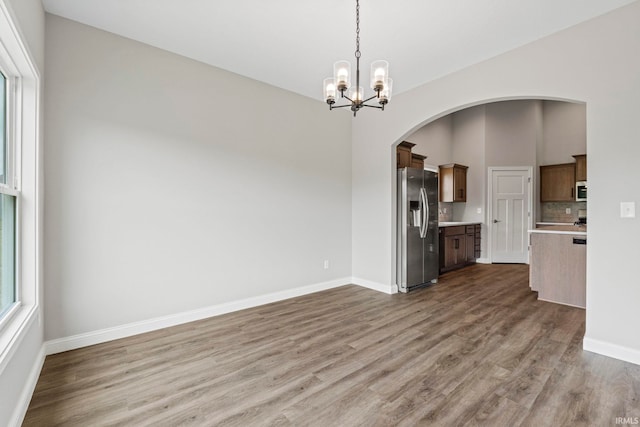 interior space featuring baseboards, arched walkways, a chandelier, and wood finished floors