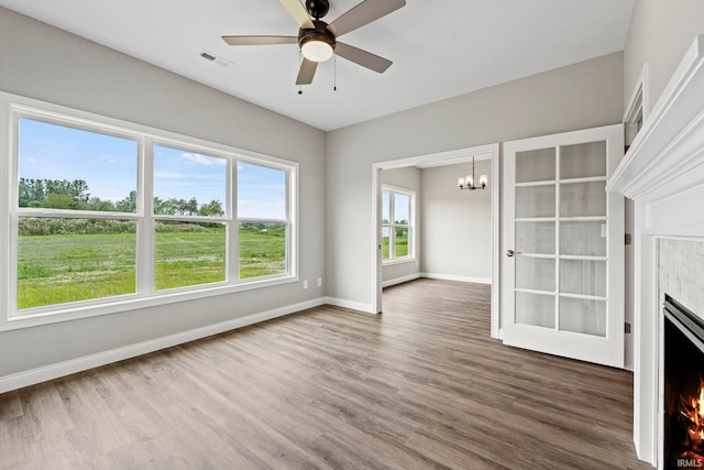 unfurnished living room with baseboards, visible vents, wood finished floors, a lit fireplace, and ceiling fan with notable chandelier