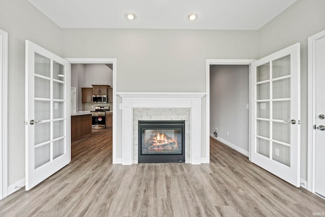 unfurnished living room featuring a stone fireplace, french doors, and light wood-style floors