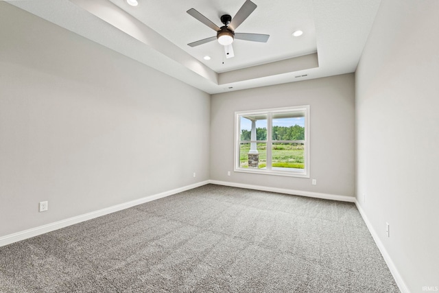 carpeted spare room featuring a tray ceiling, recessed lighting, a ceiling fan, and baseboards