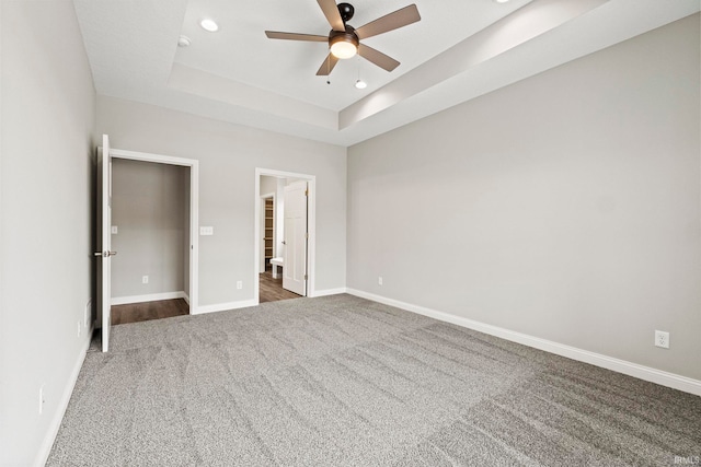 unfurnished bedroom with recessed lighting, a ceiling fan, baseboards, dark colored carpet, and a raised ceiling