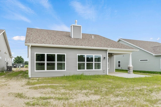 back of house featuring a shingled roof, a patio area, a lawn, and a chimney