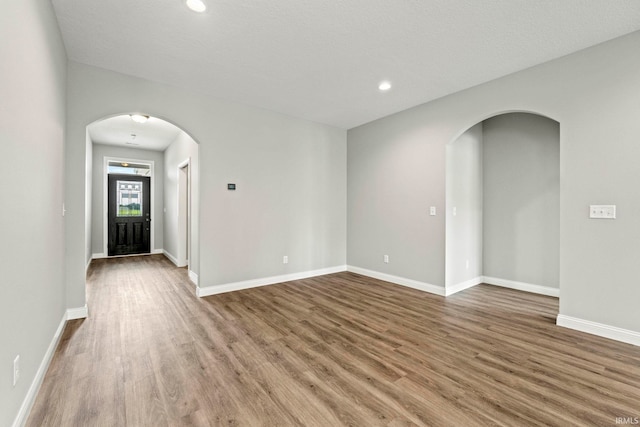 empty room with arched walkways, recessed lighting, baseboards, and wood finished floors