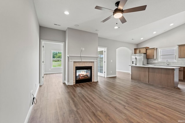 unfurnished living room featuring arched walkways, visible vents, vaulted ceiling, wood finished floors, and a multi sided fireplace