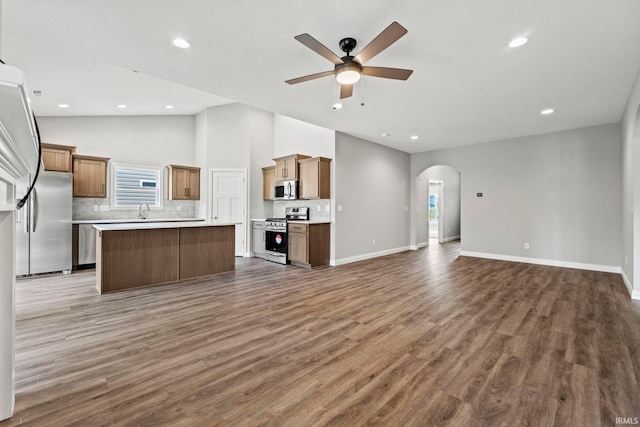 kitchen featuring dark wood-style floors, arched walkways, backsplash, appliances with stainless steel finishes, and open floor plan