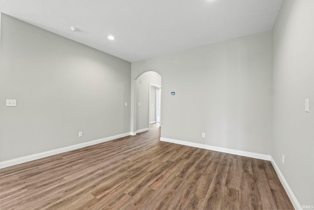 unfurnished room featuring arched walkways, recessed lighting, wood finished floors, and baseboards