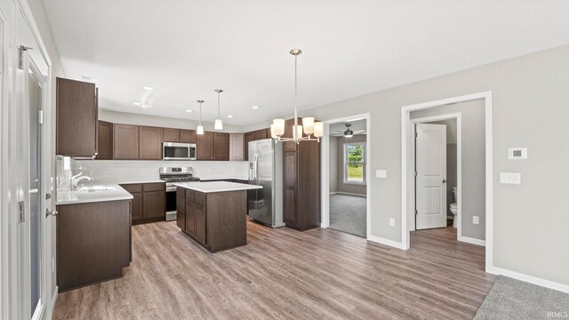 kitchen featuring a center island, dark brown cabinets, hanging light fixtures, appliances with stainless steel finishes, and backsplash