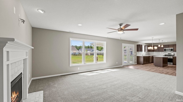 unfurnished living room featuring a tiled fireplace, light carpet, a textured ceiling, and ceiling fan