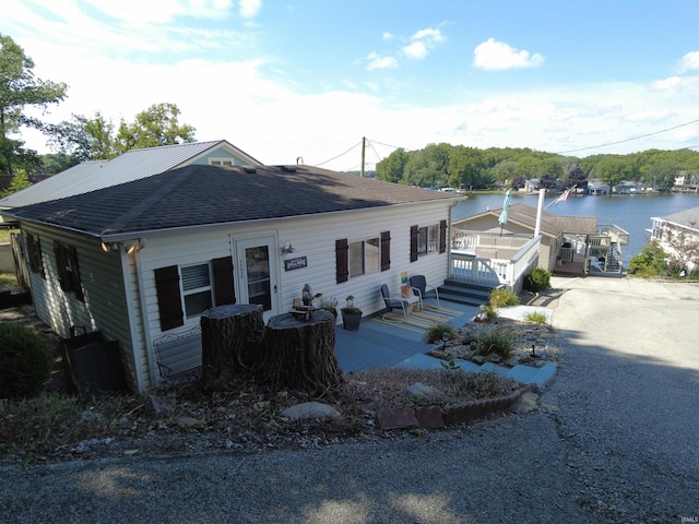 view of front of property featuring a water view, a shingled roof, and a patio